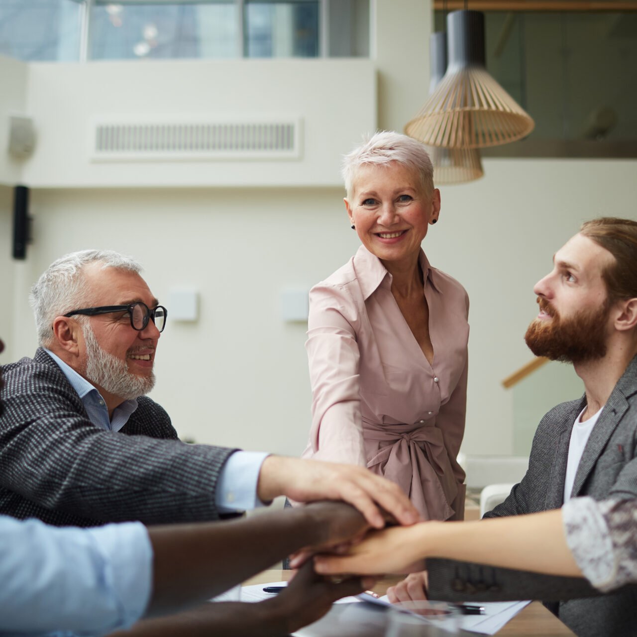 Portrait of diverse business team stacking hands while huddling over meeting table in office, copy space